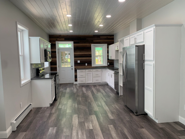 Modern kitchen with white cabinets, stainless fridge, dark countertops, and gray wood flooring.