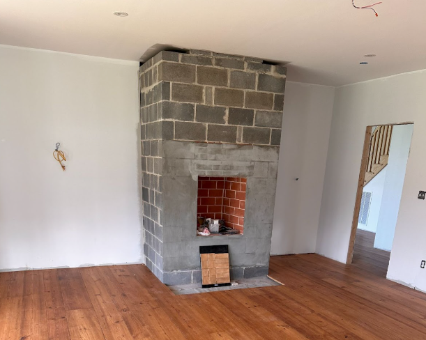 Empty living room with hardwood floors and a gray brick fireplace in the center