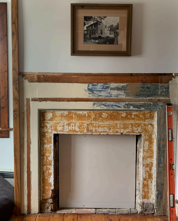 Damaged fireplace surround with peeling paint and a framed photo above it in a room