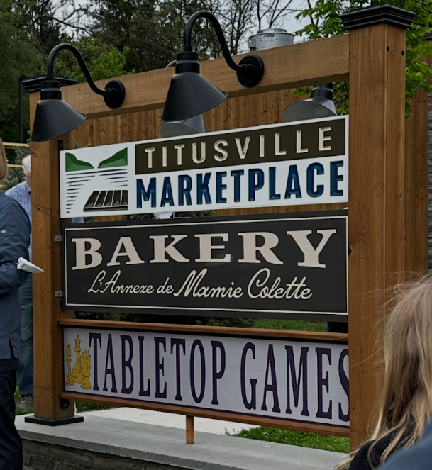 Outdoor sign for Titusville Marketplace, bakery, and tabletop games in a wooden frame