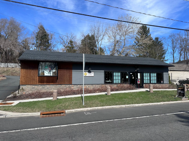 Single-story brown-and-gray building with large windows beside a road under a blue sky