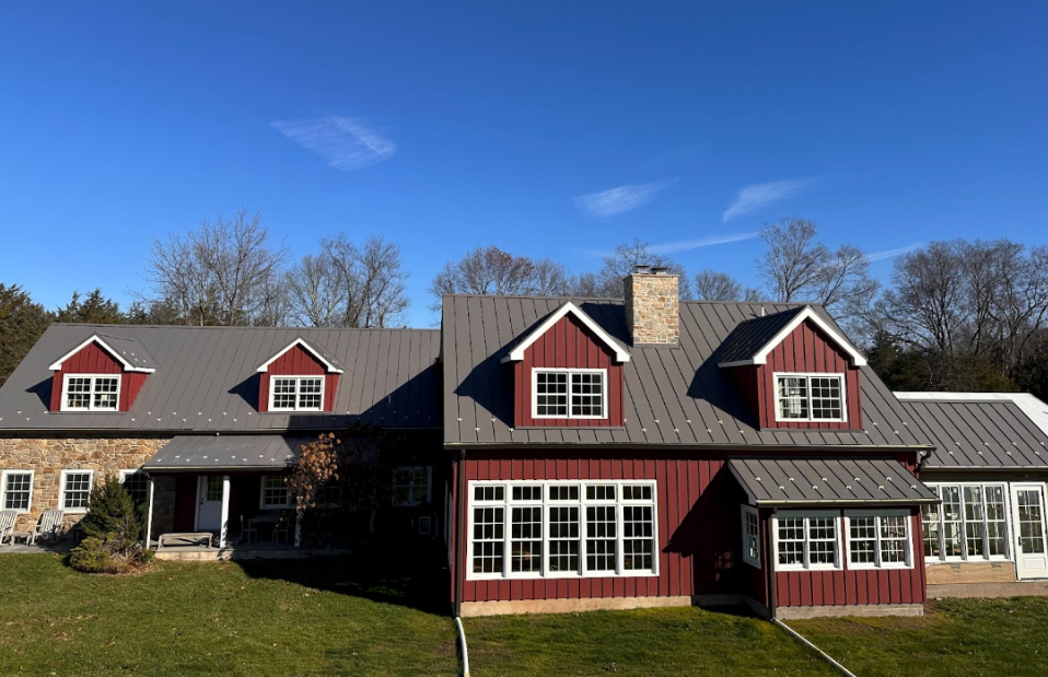 Large red farmhouse with gray roofs and white-trimmed windows under a clear blue sky