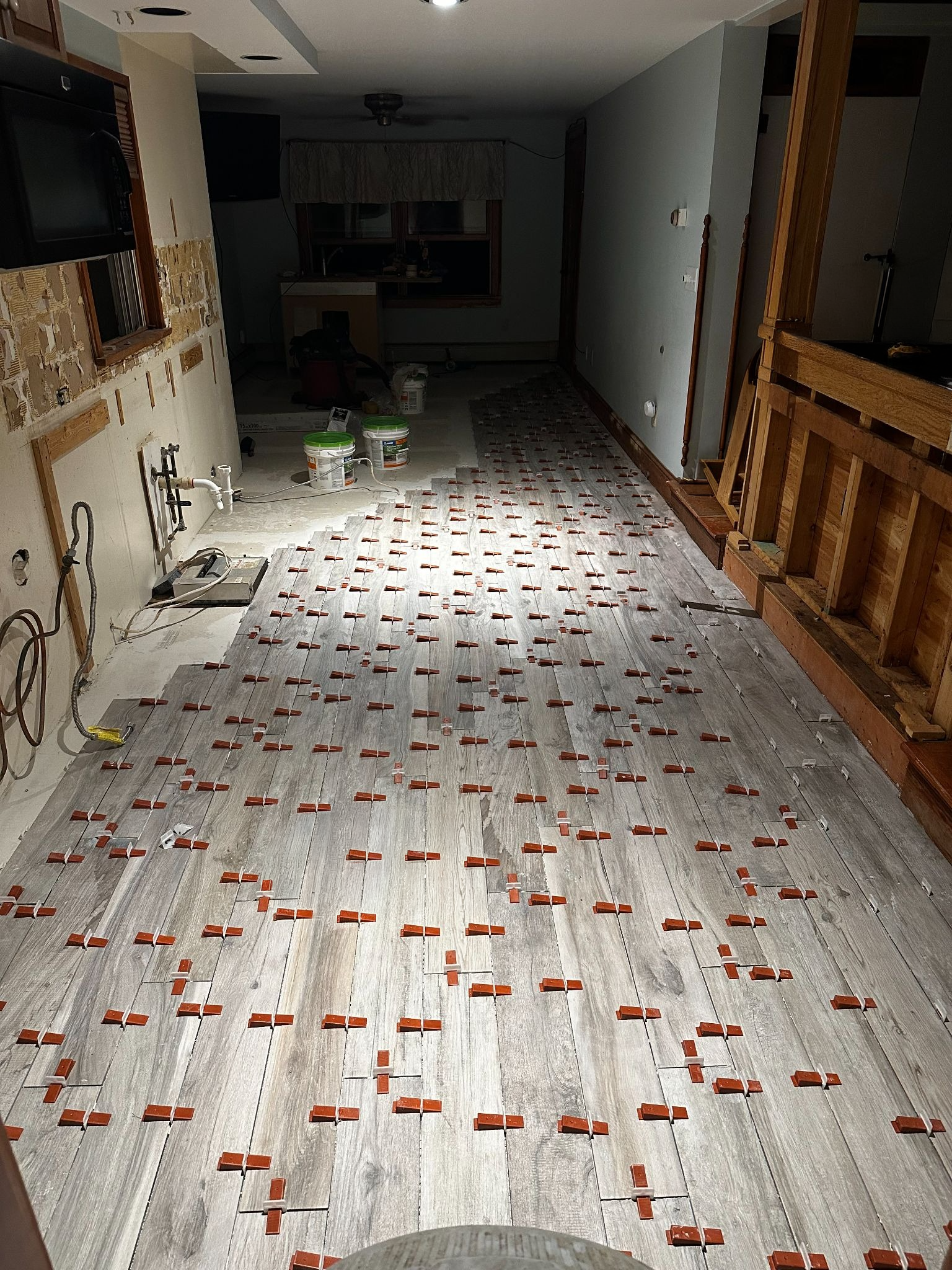 Long hallway with a damaged floor covered in debris and scattered tiles, leading to a dark room.