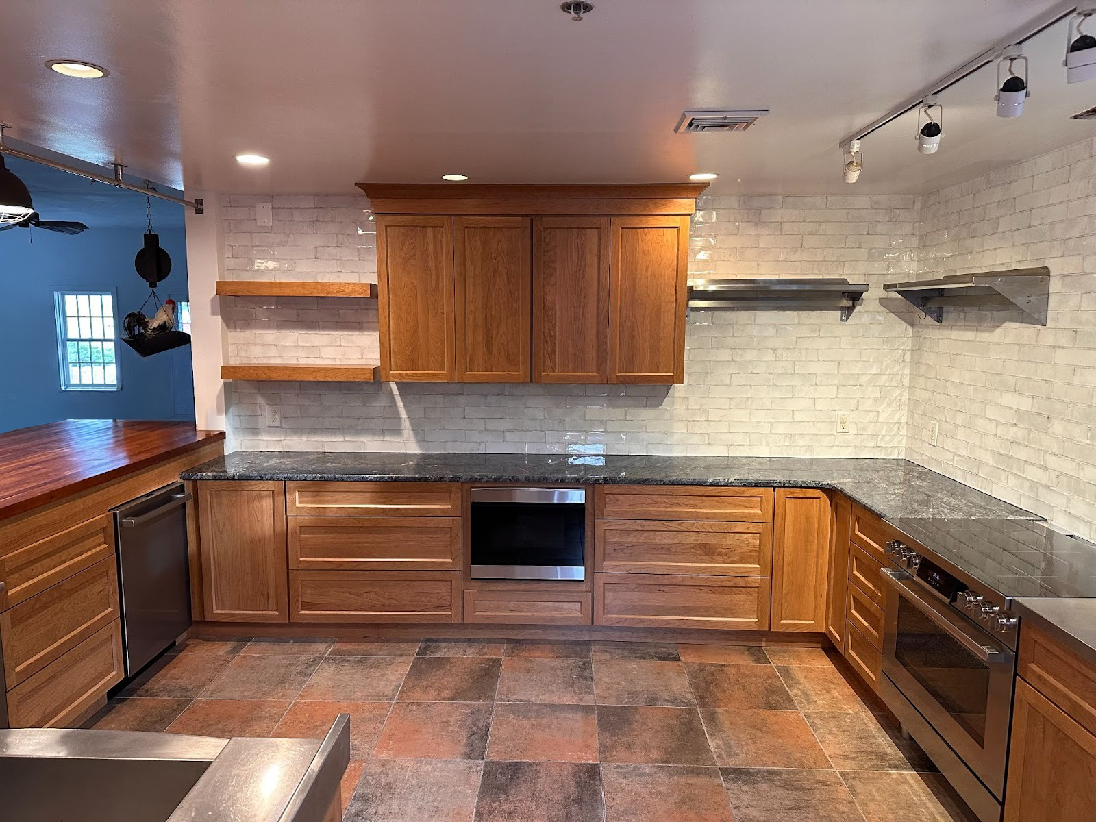 Empty kitchen with wood cabinets, beige tile backsplash, and brown tile floor under ceiling track lighting