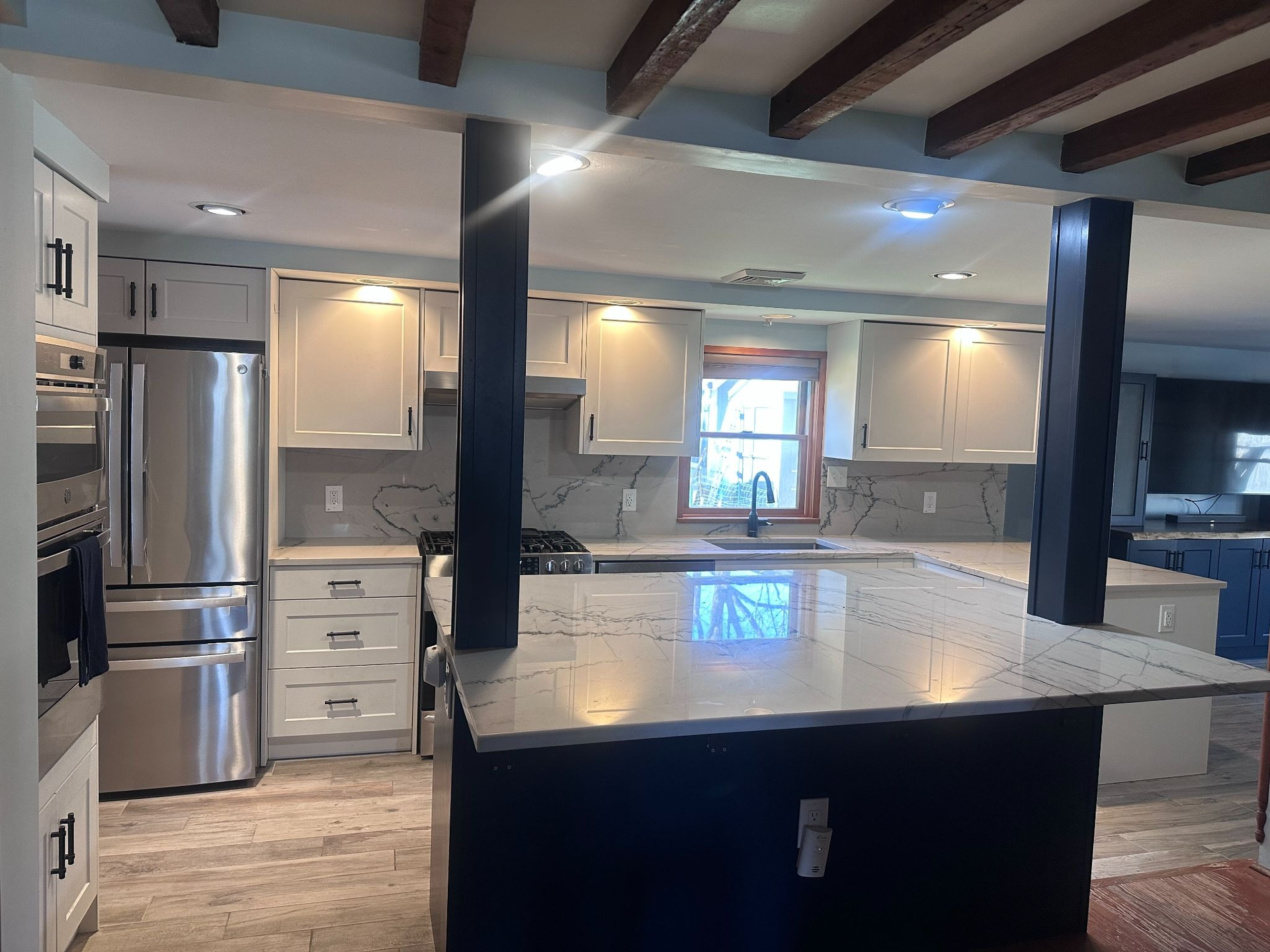 Modern kitchen with white cabinets, stainless steel fridge, island, and exposed dark ceiling beams