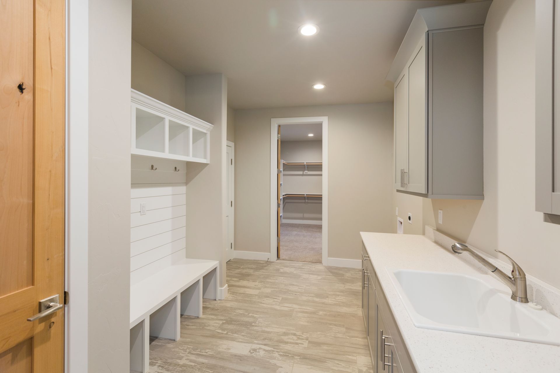 Bright laundry room with white cabinets, sink, bench, and beige tile floor leading to a doorway.