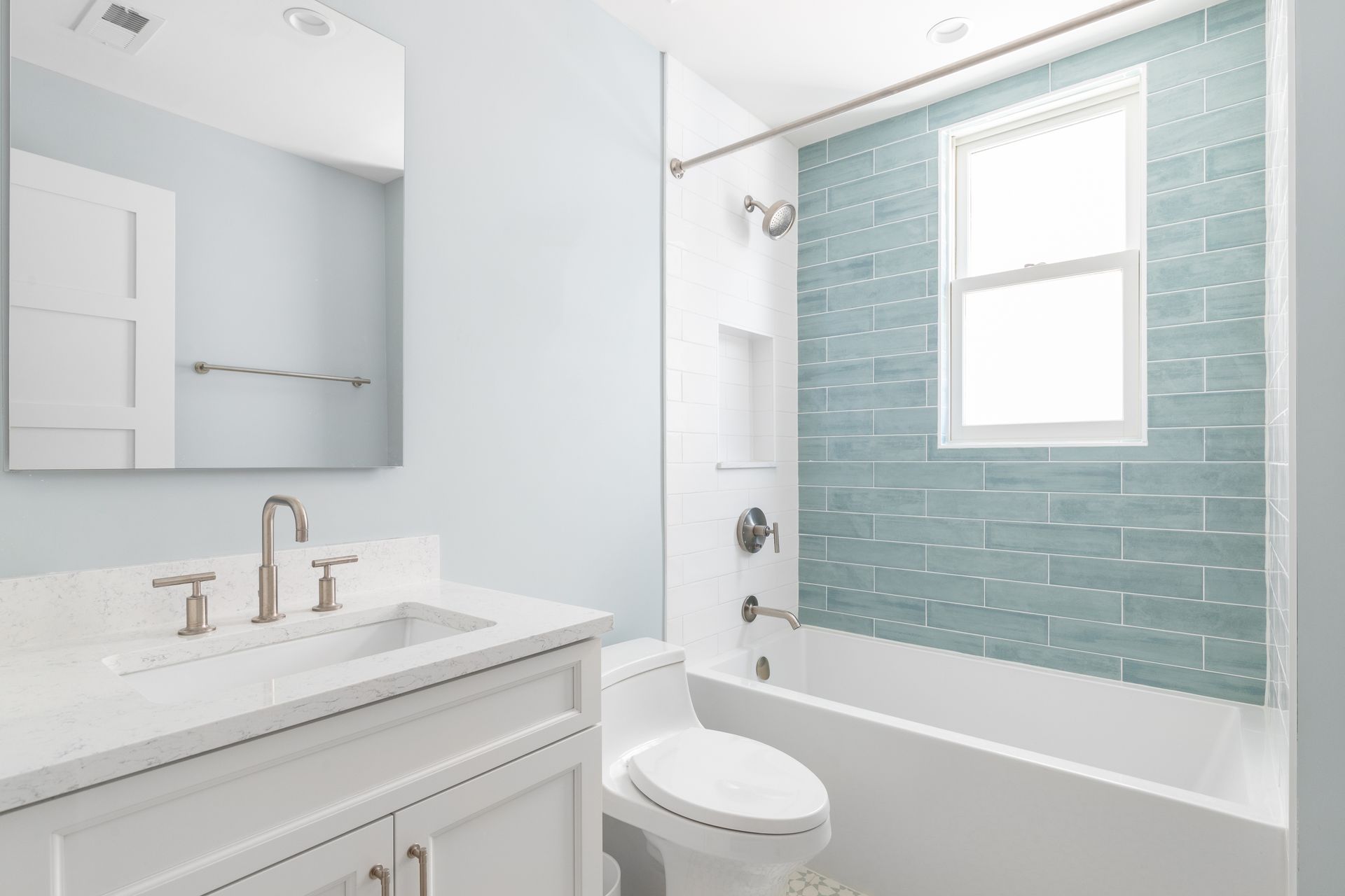 Bright white bathroom with marble vanity, mirror, toilet, and tub with blue tiled shower wall