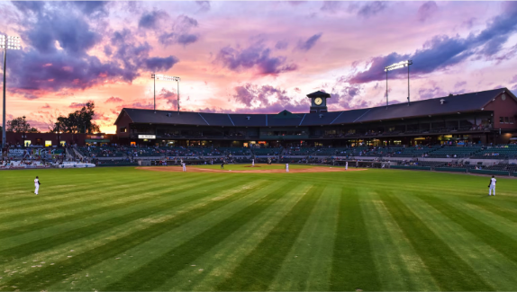 Baseball stadium at sunset with green striped field and pink-purple sky