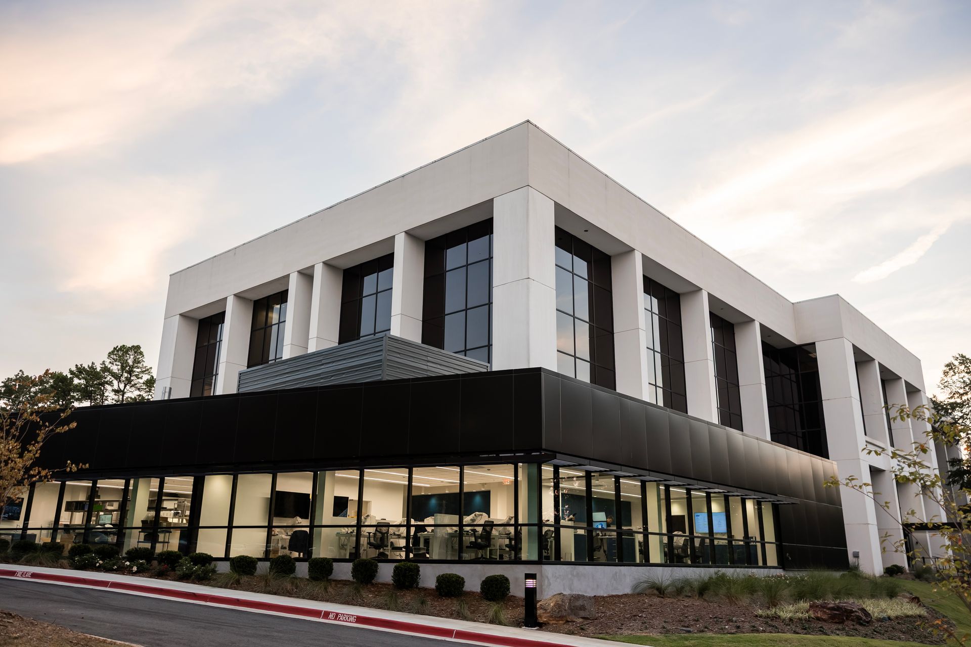 Modern white office building with black glass storefront and landscaped entrance at dusk