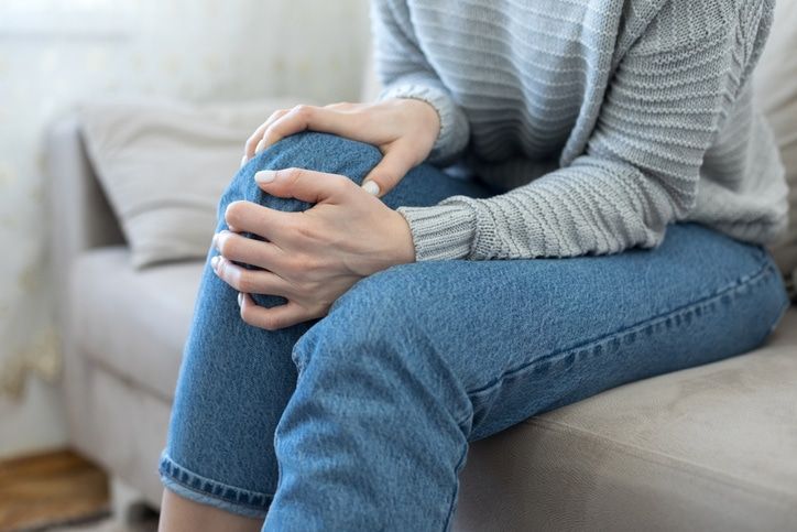 a woman is sitting on a couch holding her knee in pain