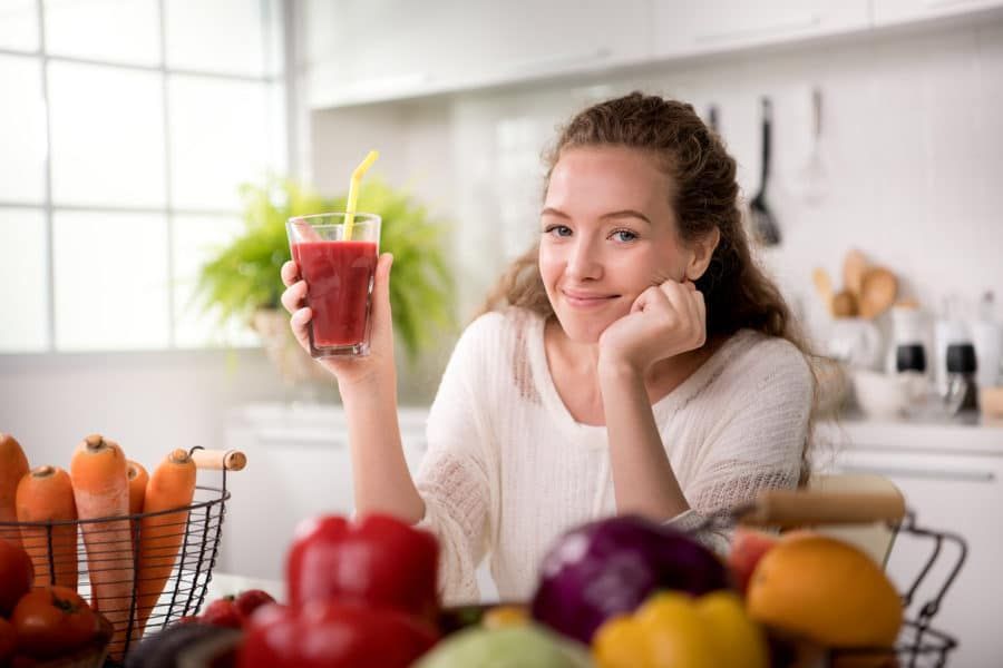 a woman is holding a glass of juice in a kitchen