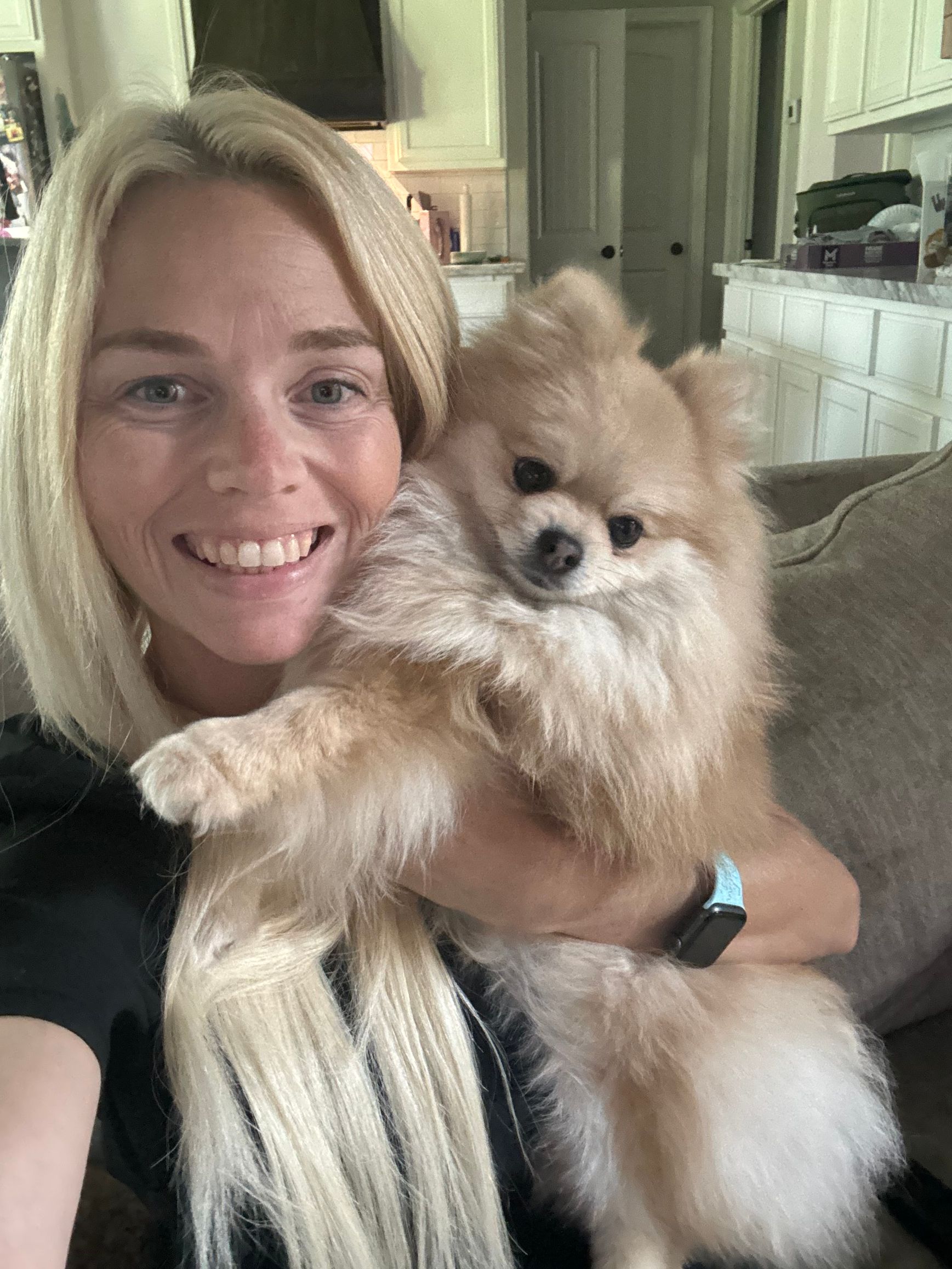A woman is sitting on a couch holding a small dog.