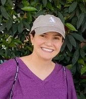 A woman wearing a baseball cap and a purple shirt is smiling.