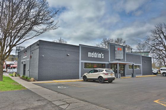 Modern gray storefront with white lettering, parked SUV, and leafless trees on a cloudy day