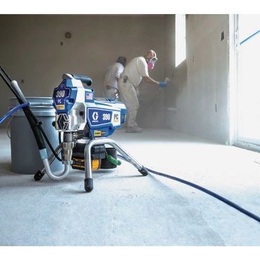 Workers spraying white coating on a wall in a room, with paint sprayer equipment in the foreground