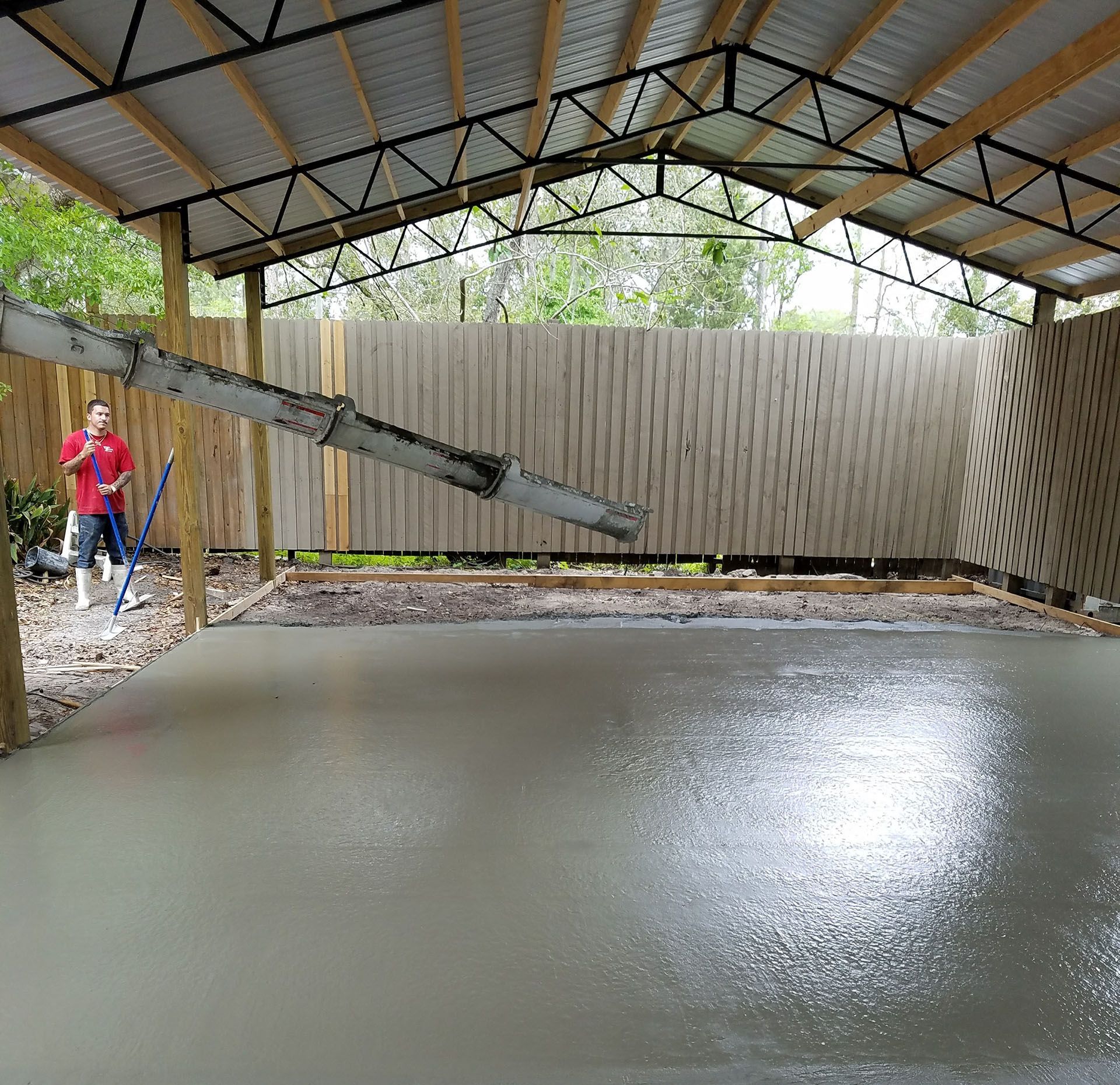 Freshly poured concrete slab under a roofed structure, with workers smoothing the surface.
