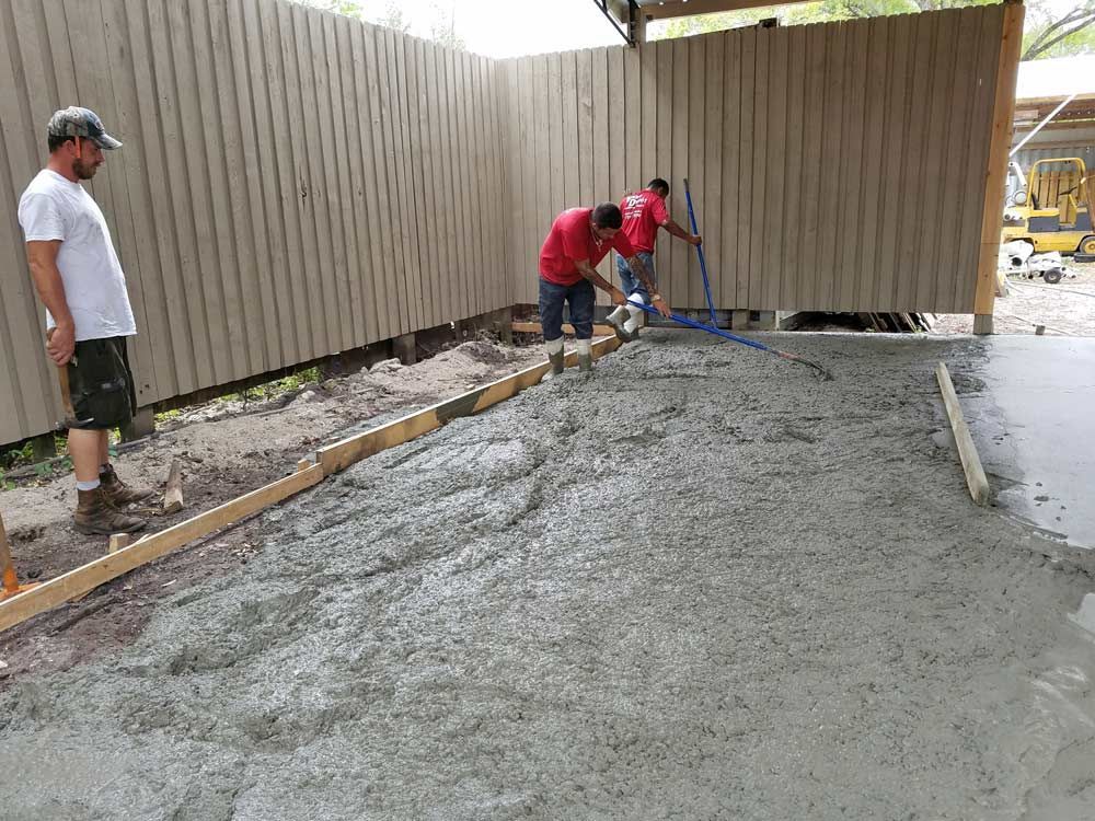 Workers pouring and smoothing wet concrete in a fenced outdoor area