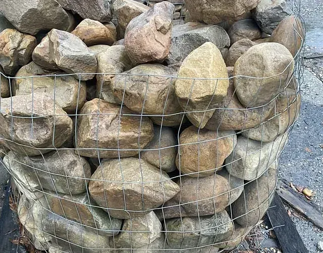 Wire mesh cage filled with stacked tan rocks outdoors
