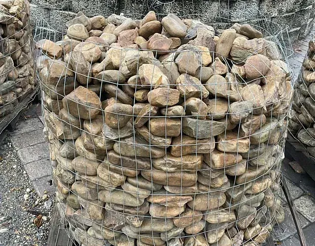 Wire mesh cage filled with tan rocks or pavers stacked outdoors on pavement.