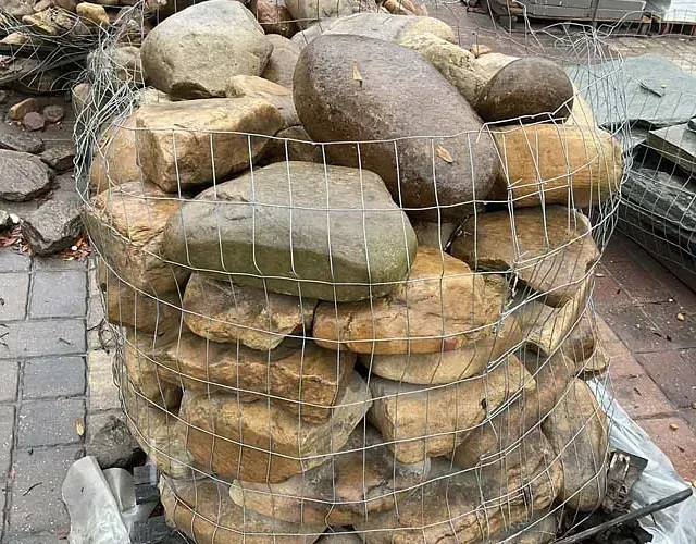 Wire basket filled with assorted smooth stones and rocks on a paved surface