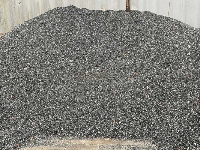 Large pile of gray gravel or crushed stone stacked outdoors against a wall
