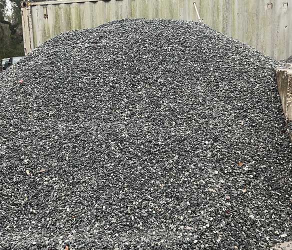 A large pile of crushed gray gravel in front of a corrugated metal wall.