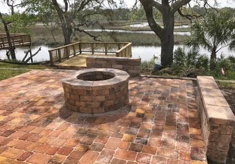 Brick patio with a circular fire pit overlooking a river and trees