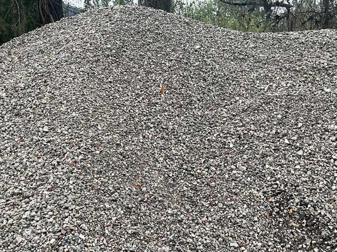 Large pile of gray gravel outdoors with trees in the background