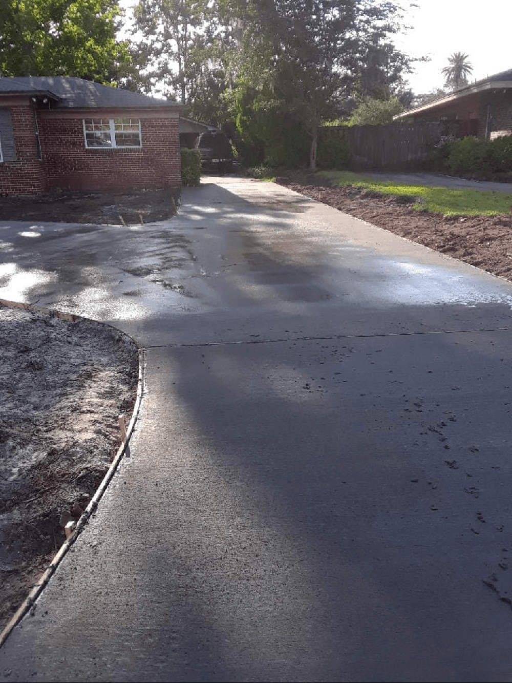 Wet driveway beside brick houses after rain, with sunlight and wet pavement reflections