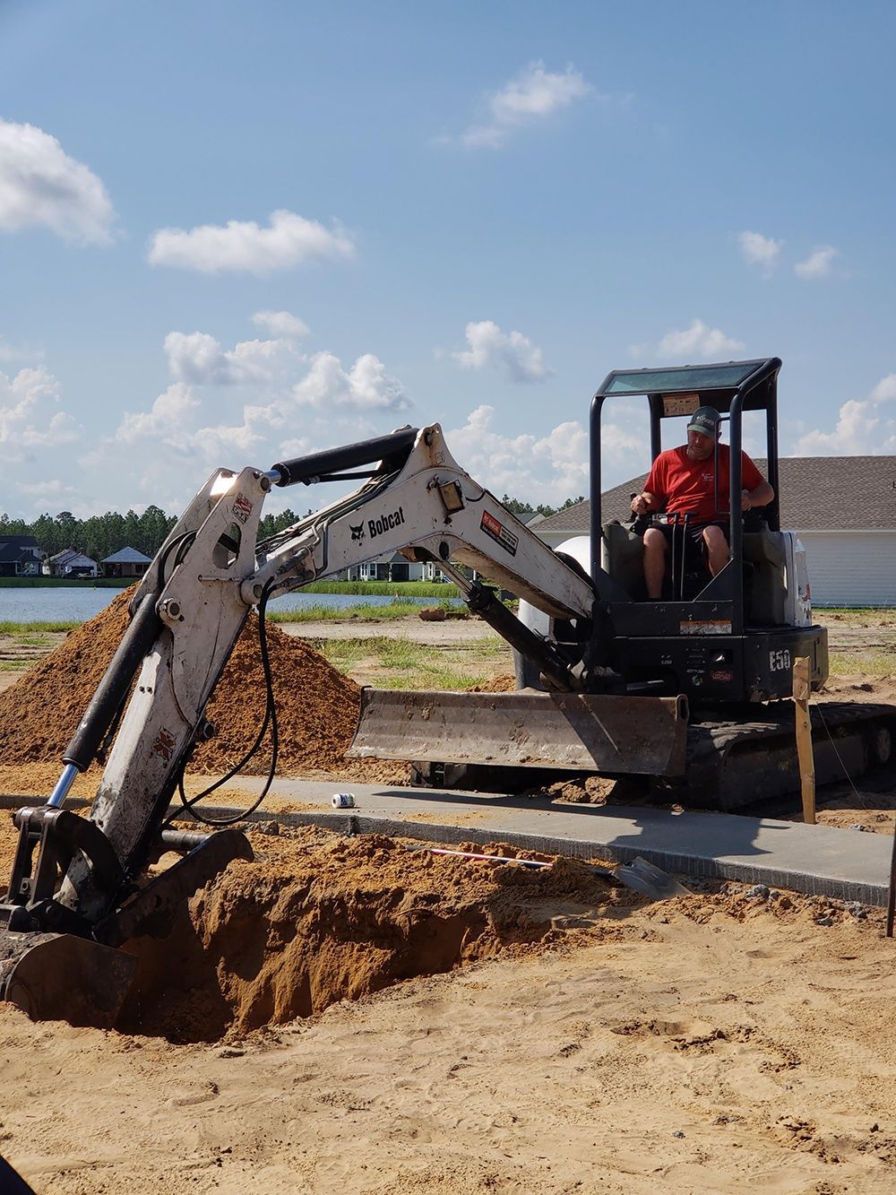 Small excavator digging soil beside a paved road under a blue sky