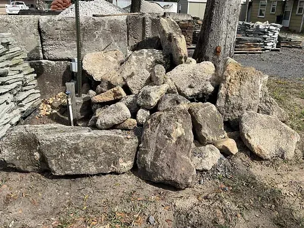 Pile of large gray rocks stacked outdoors beside a yard and house.
