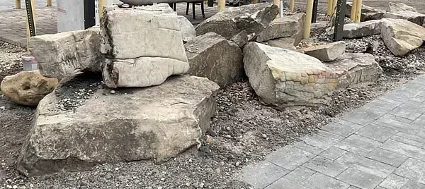 Large decorative rocks beside a paved walkway in an outdoor plaza.