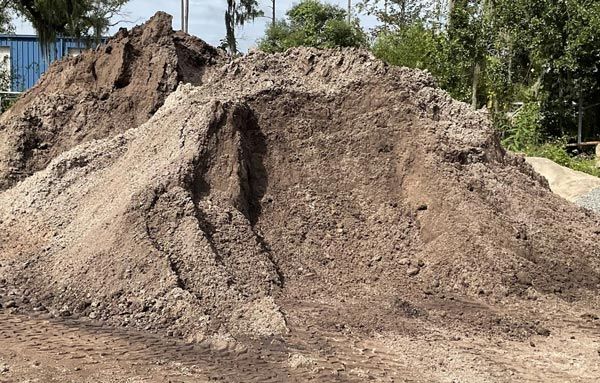 Large dirt mound at a construction site with trees in the background