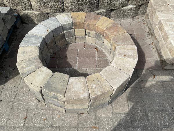 Circular stone fire pit built with light gray pavers on a brick patio.