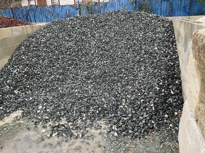 Large pile of dark gravel or crushed rock in a concrete storage area.
