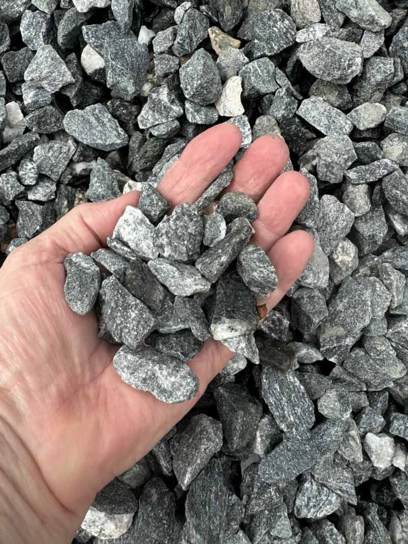 Hand holding gray crushed stone gravel over a pile of similar rocks