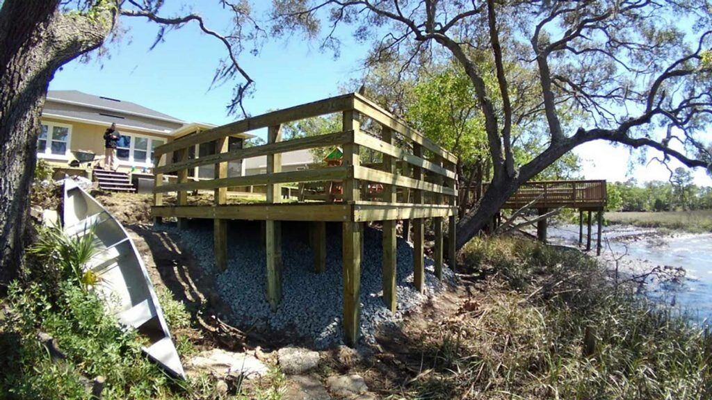 Wooden deck on stilts beside a lakeside house, with trees and water in the background