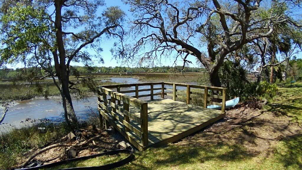 Wooden viewing deck by a river under trees on a sunny day