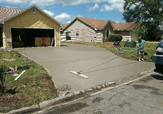 Suburban driveway under construction beside a garage, with a worker and a truck on a sunny day