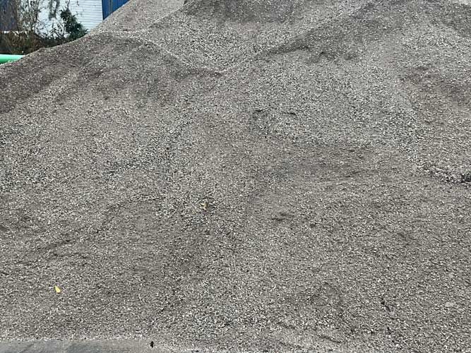Large gray gravel pile in an outdoor area, with a bit of greenery at the edge