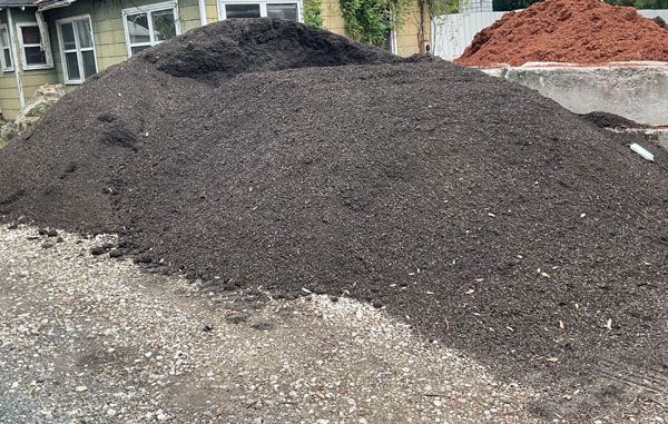 Large pile of dark gravel or soil at a construction site, with a smaller red pile in the background.