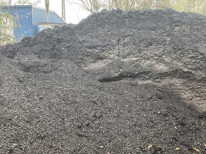 Large pile of dark gravel or coal outdoors, with a blue structure in the background