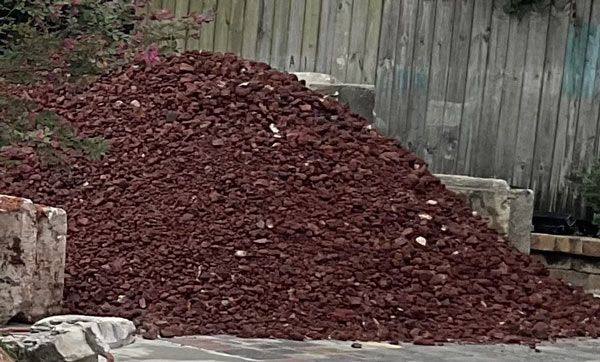 Large pile of red mulch or wood chips beside a weathered wooden fence.