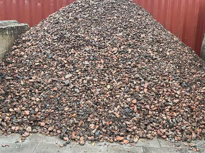 Large pile of brown gravel or rocks in front of a red fence and concrete path