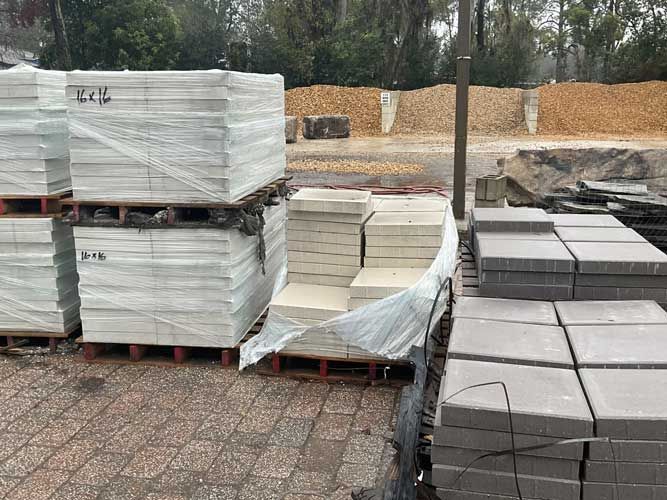 Stacks of wrapped concrete pavers on pallets in an outdoor storage yard.