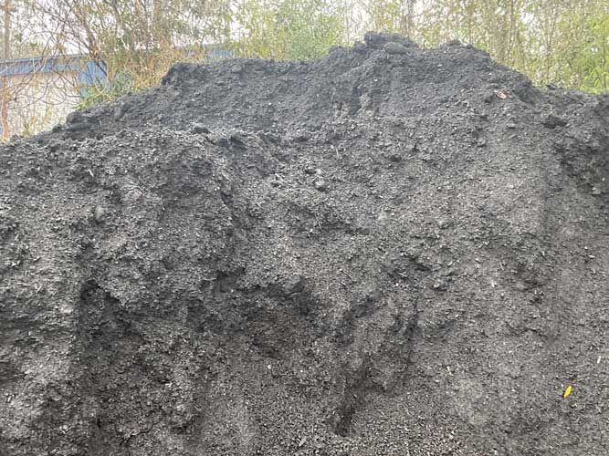 Large dark gravel pile outdoors with trees in the background