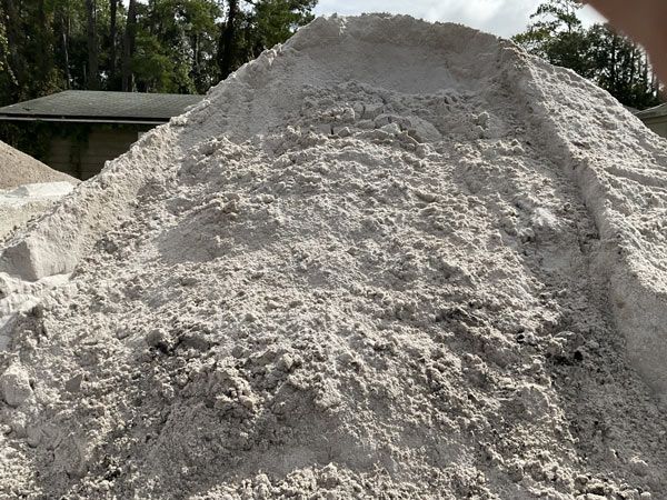 Large pile of gray sand or gravel outdoors beside a small building and trees