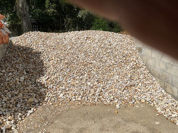 Pile of light-colored gravel or crushed stone beside a concrete wall outdoors.