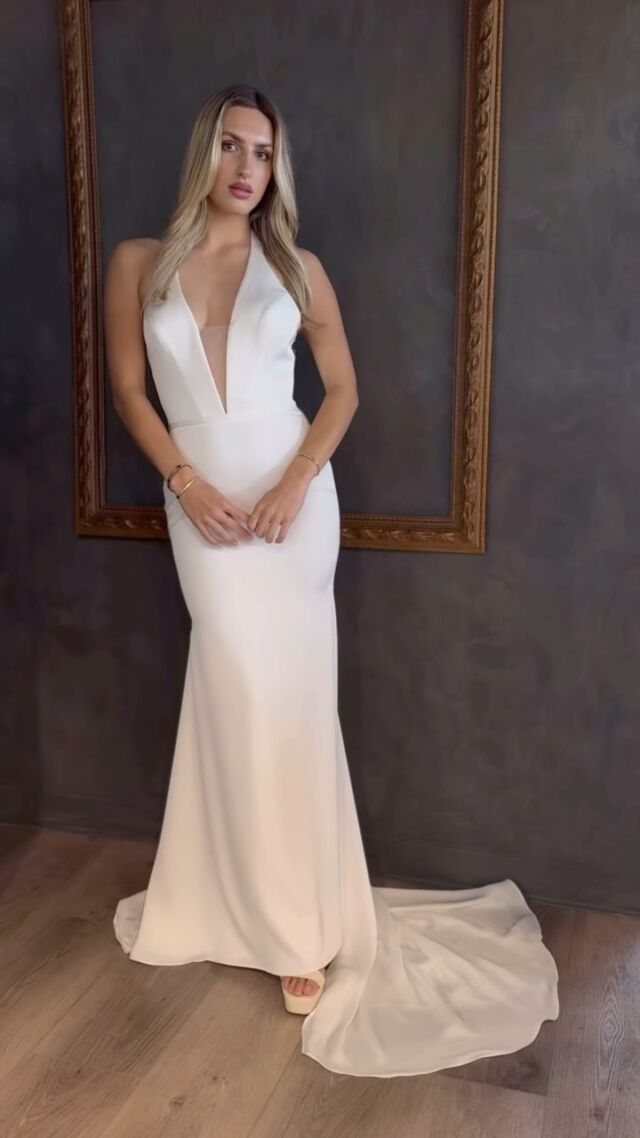 A woman in a white dress is standing in front of a mirror.
