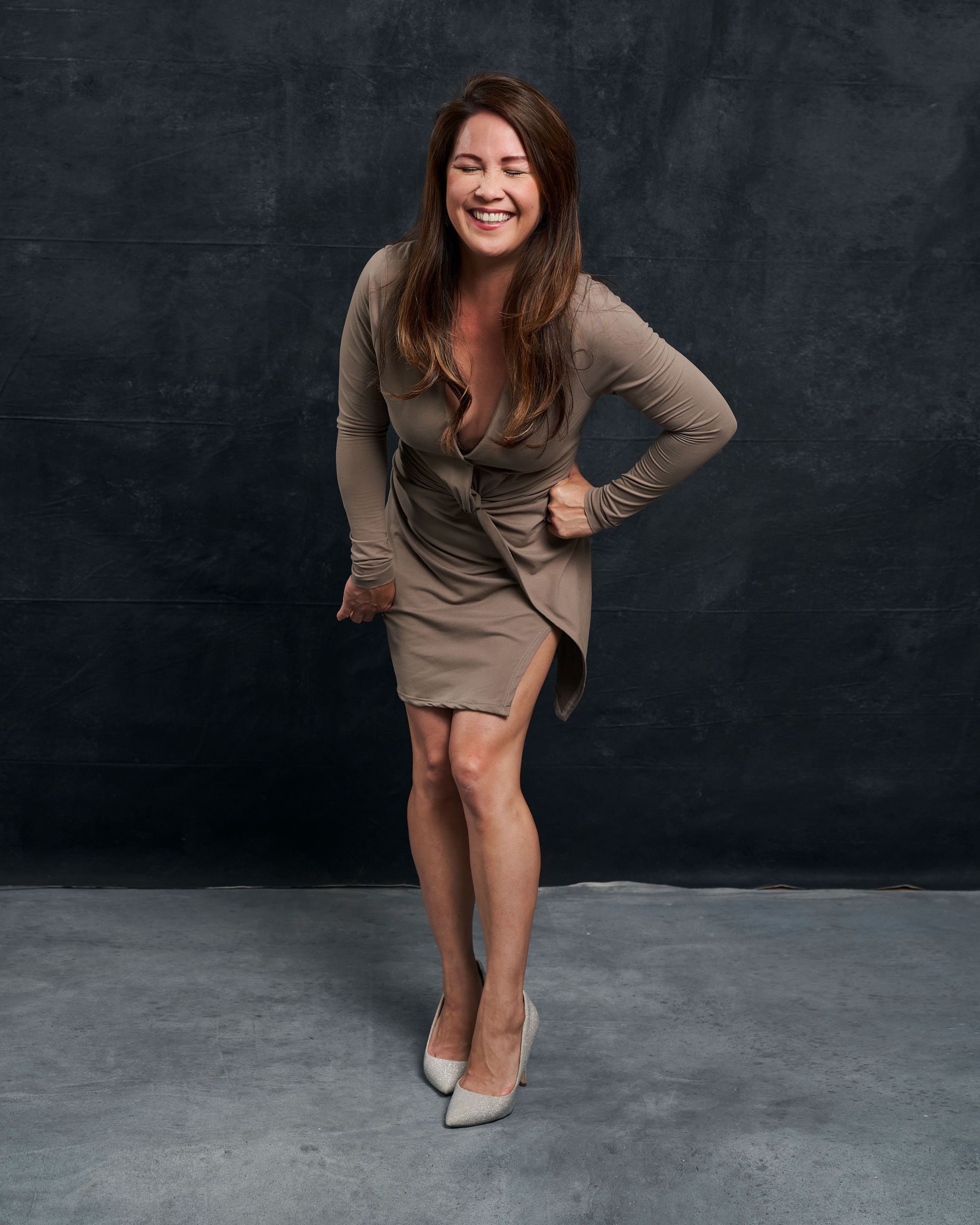 A woman in a dress is standing in front of a black wall and smiling.